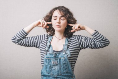 Kadın kulaklarını elleriyle, parmaklarıyla kapatıyor. Gri arkaplan