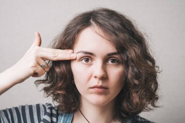 İntihar jesti yapan kadın, şakağına işaret parmağı, hayali bir silah. Gri arkaplan