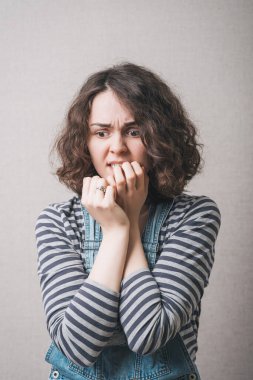 Kadın, korku deneyimlerinde tırnaklarını yer. Gri bir arkaplanda.