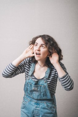 Eli kulağında olan kadın duyamaz. Gri bir arkaplanda.