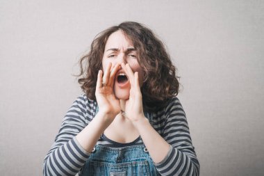 Elleri ağzının yanında bağıran bir kadın. Gri bir arkaplanda.