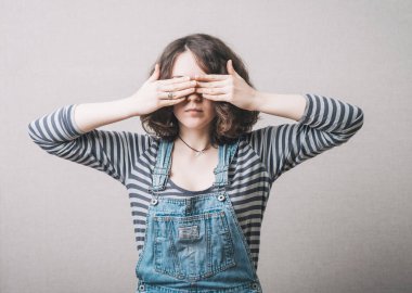 Kadın elleriyle gözlerini kapadı. Gri bir arkaplanda.