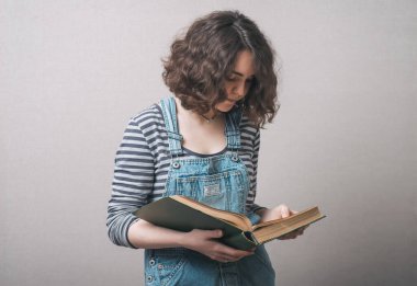 Gri bir arka planda, elinde büyük bir kitap olan kız.