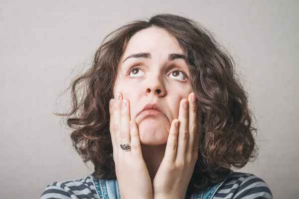 Droevige Vrouw Kijkt Met Handen Haar Wangen Een Grijze Achtergrond — Stockfoto