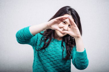 Kıvırcık kız parmaklarının arasından bakıyor. Gri arkaplan.