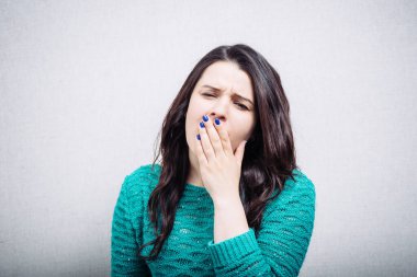 Gri arka planda esneyen genç bir kadın.