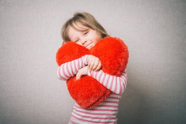 Tatlı küçük kız sevgililer günü kalbini tutuyor ve aşkı düşünüyor, gri arka planda izole edilmiş.