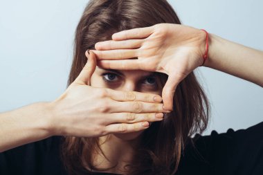 Mutlu tatlı esmer kız gözler için el çerçevesi yapıyor.