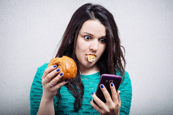 милая девушка ест кекс и держит телефон
