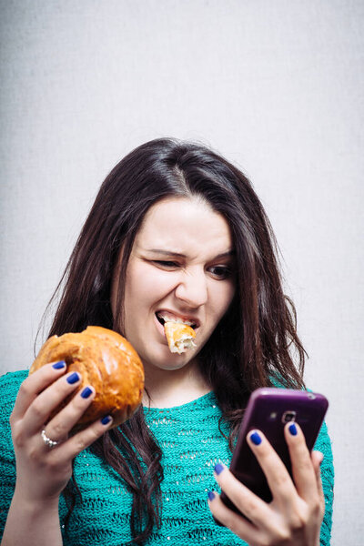 милая девушка ест кекс и держит телефон
