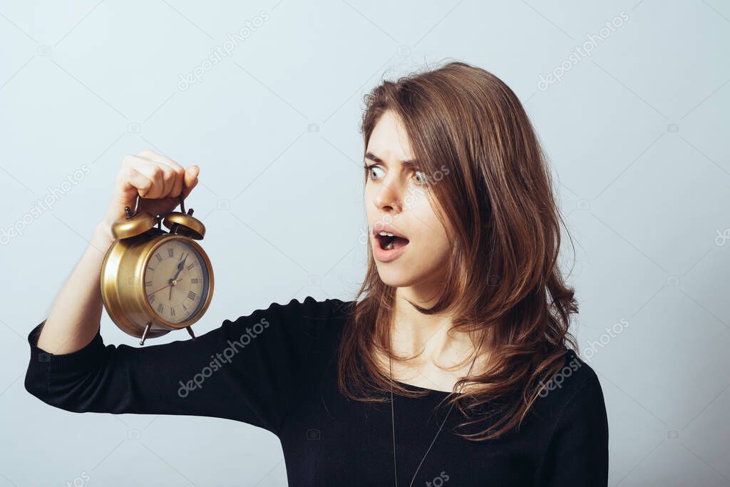 cute brunette girl slept with horror looks at an alarm clock