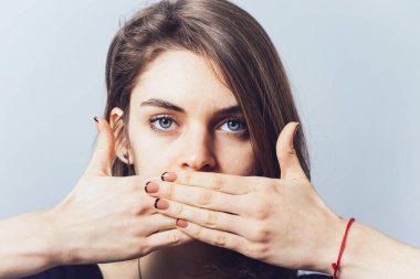 Mavi gözlü esmer kız elleriyle ağzını kapatıyor.