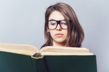 Gözlüklü kız kitap okuyor, ona bakıyor.