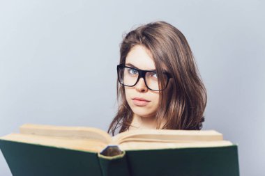 Gözlüklü kız kitap okuyor, ona bakıyor.