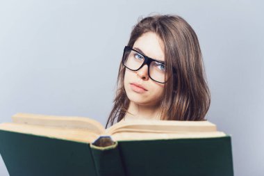 Gözlüklü kız kitap okuyor, ona bakıyor.