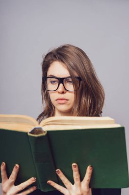 Gözlüklü kız kitap okuyor, ona bakıyor.
