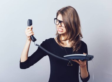 Ofisi ya da ev telefonu olan kadın küfrediyor, çığlık atıyor. Gri bir arkaplanda.