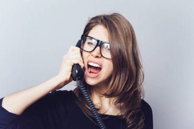 Ofisi ya da ev telefonu olan kadın küfrediyor, çığlık atıyor. Gri bir arkaplanda.