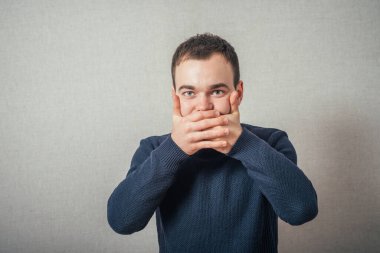 Adam onun elleriyle ağzını kapattı. Gri bir arkaplanda.