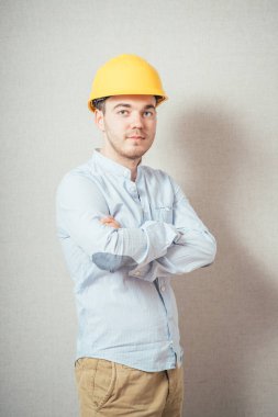 Sarı kasklı adam kollarını göğsüne kadar katladı. Gri bir arkaplanda.