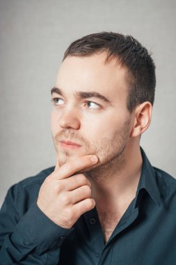 Adam elleri başının yanındayken üzgün olduğunu düşünüyor. Gri bir arkaplanda.