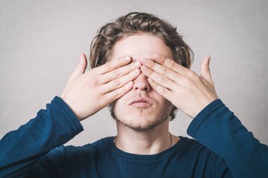 Adam elleriyle gözlerini kapadı. Gri bir arkaplanda.