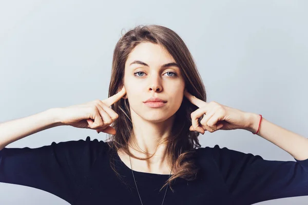 girl covers her ears on a gray background