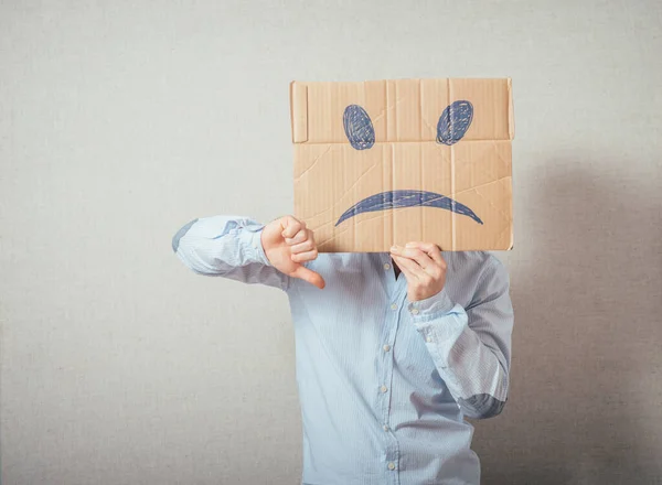 Young man with an unhappy smiley card half covering face