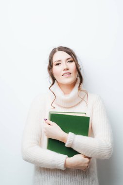 Elinde büyük bir kitapla beyaz bir arka planda esmer bir kız.