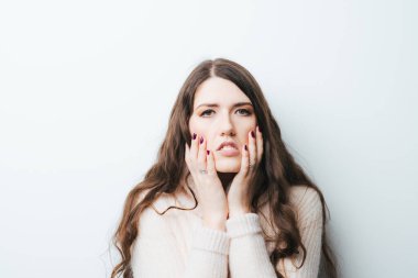 Kafası karışmış kadın ellerini yanaklarına koyar, beyaz tenli.