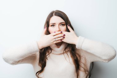 Beyaz bir arka planda uzun saçlı genç bir kız elleriyle ağzını kapatıyor.