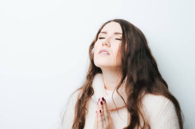 Beyaz bir arka planda uzun saçlı genç bir kız dua ediyordu.