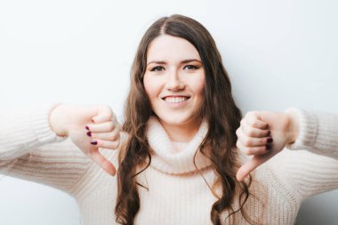 Beyaz arka planda uzun saçlı genç bir kız baş parmağını aşağı gösteriyor.