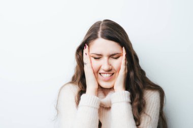 Güzel, uzun saçlı bir kızın başı ağrıyordu ve ellerini beyaz bir arka planda tutuyordu.