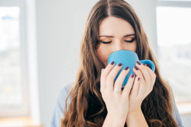 Pencerenin yanında bir fincan çayla genç bir kadının portresi.