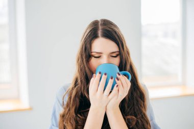 Pencerenin yanında bir fincan çayla genç bir kadının portresi.