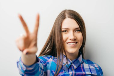 Mutlu gülümseyen güzel genç kadın iki parmak ya da zafer işareti gösteriyor, beyaz arka planda izole edilmiş.