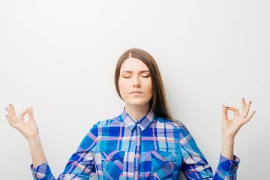 Beyaz bir arka planda genç bir kız meditasyon yapıyor.