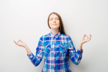 Beyaz bir arka planda genç bir kız meditasyon yapıyor.