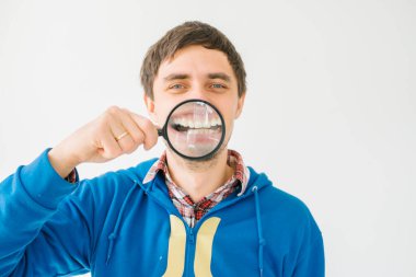 Gri bir arka planda büyüteçle genç bir adam.