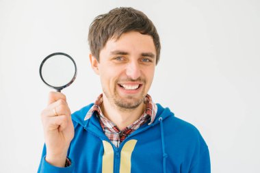 Gri bir arka planda büyüteçle genç bir adam.