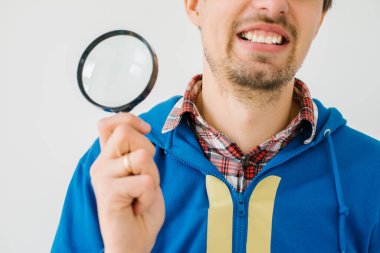 Gri bir arka planda büyüteçle genç bir adam.