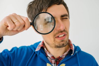 Gri bir arka planda büyüteçle genç bir adam.