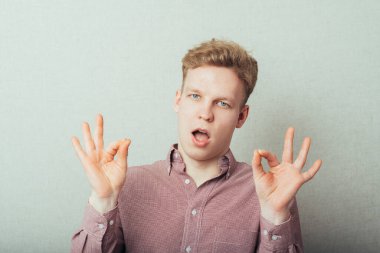 Tamam işareti işaretleniyor. Gömlekli ve kravatlı neşeli genç adam. Gri arka planda dururken işaret veriyor.