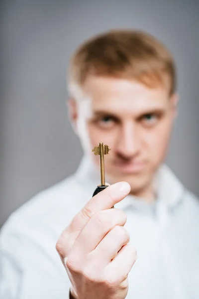 Man wearing a  shirt looking happy holding a rusty key.