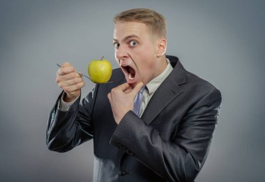 Genç, mutlu ve aç adam çatalda elma tutuyor. 