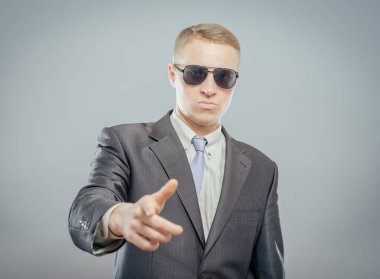 Sırada sen varsın! Güneş gözlüklü genç iş adamları gri üzerinde izole bir şekilde kamerayı işaret ediyorlar.