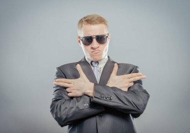 Güneş gözlüklü yakışıklı genç adam silah şeklinde kollarını kavuşturdu. Jest yap. İzole edilmiş sarı arka plan. fotoğraf