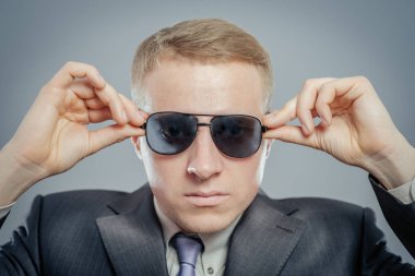 Açık gri takım elbiseli ve kravatlı bir iş adamı izole edilmiş. Siyah güneş gözlüğü takıyordu. Stüdyo çekimi.