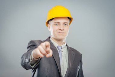 Sarı kasklı genç adam parmağıyla birini işaret ediyor.